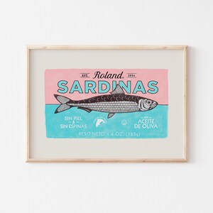 May include: A vintage-style illustration of a sardine can label. The label is pink and blue with black text and a black and white illustration of a sardine. The text reads "Est. Roland 1914 Sardinas Sin Piel & Sin Espinas En Aceite De Oliva Peso Neto 4.4 Oz. (125g)"