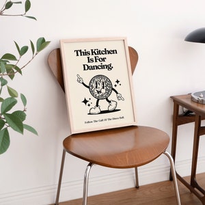 May include: A framed print with the text "This Kitchen Is For Dancing" and a cartoon disco ball character. The print is displayed on a wooden chair. The image has a retro, vintage aesthetic.