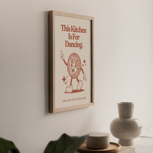 May include: A framed print with a brown background and a cartoon disco ball character dancing. The text reads "This Kitchen Is For Dancing. Follow The Call Of The Disco Ball."