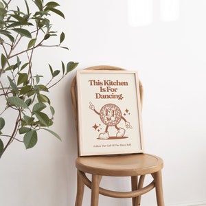 May include: A framed print with a brown background and white text that reads "This Kitchen Is For Dancing." A cartoon disco ball with a smiling face is dancing with its arms outstretched. The text "Follow The Call Of The Disco Ball." is at the bottom of the print.