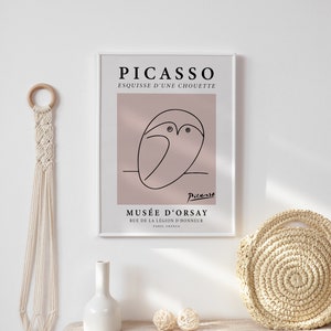 Puede incluir: Un cuadro enmarcado de Picasso con un boceto de b&uacute;ho en l&iacute;neas negras sobre un fondo rosa. La impresi&oacute;n incluye el texto "PICASSO ESQUISSE D'UNE CHOUETTE" y "MUS&Eacute;E D'ORSAY". Un colgante de pared de macram&eacute;, un jarr&oacute;n blanco y una cesta tejida tambi&eacute;n son visibles.