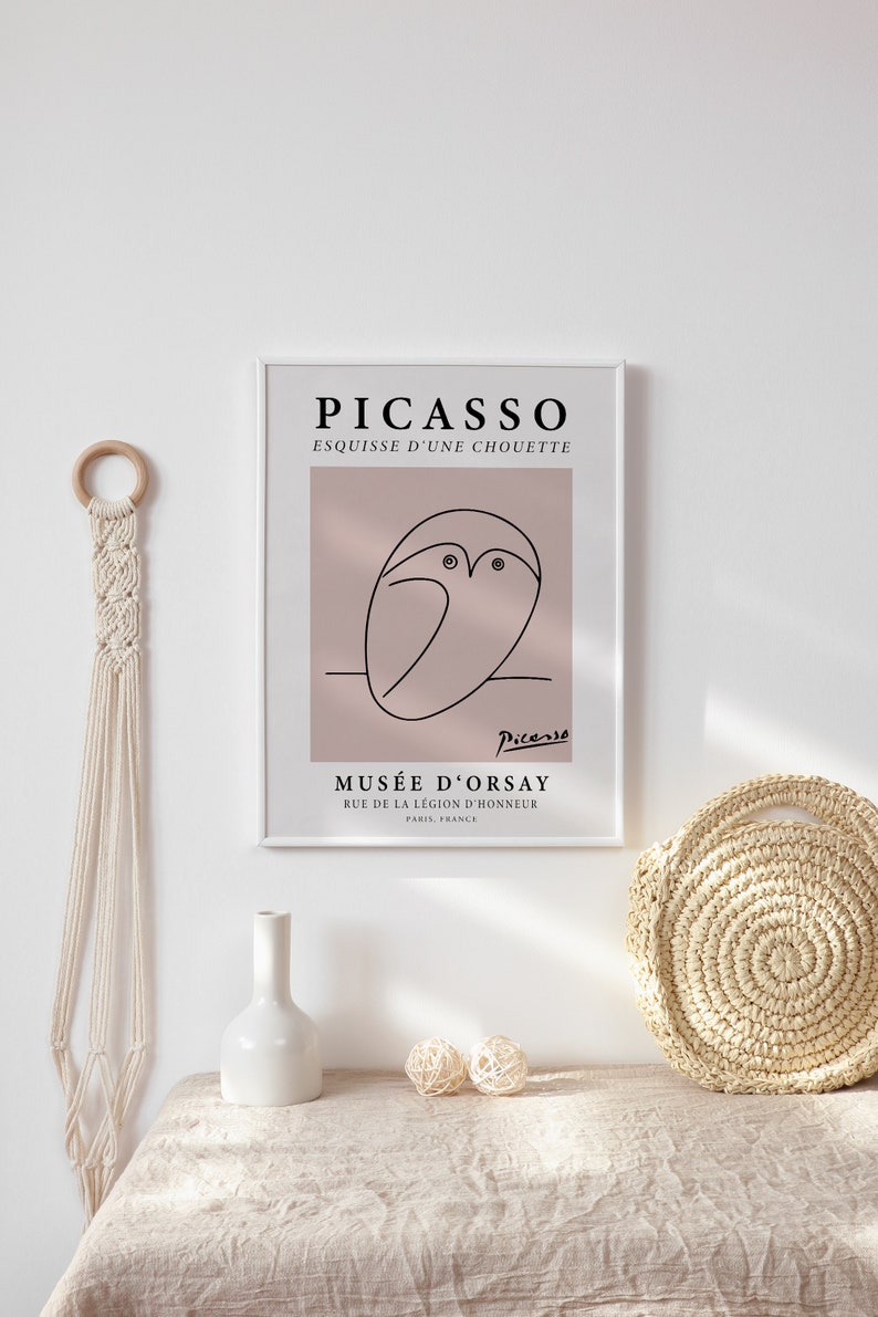 Puede incluir: Un cuadro enmarcado de Picasso con un boceto de b&uacute;ho en l&iacute;neas negras sobre un fondo rosa. La impresi&oacute;n incluye el texto "PICASSO ESQUISSE D'UNE CHOUETTE" y "MUS&Eacute;E D'ORSAY". Un colgante de pared de macram&eacute;, un jarr&oacute;n blanco y una cesta tejida tambi&eacute;n son visibles.