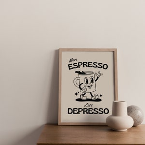 May include: A framed print with the words "More Espresso Less Depresso" and a cartoon coffee cup character. The artwork is in black and beige tones, with a wooden frame. The print is displayed on a wooden cabinet.