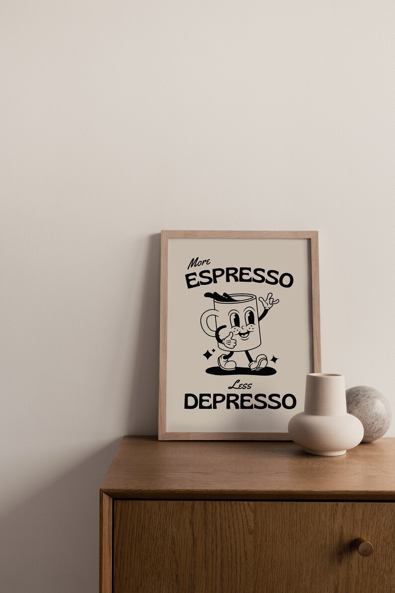 May include: A framed print with the words "More Espresso Less Depresso" and a cartoon coffee cup character. The artwork is in black and beige tones, with a wooden frame. The print is displayed on a wooden cabinet.