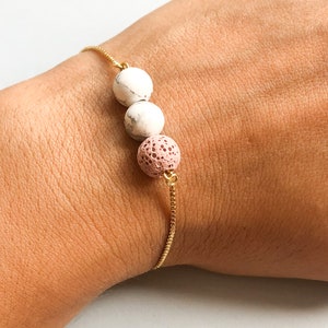 Könnte beinhalten: Ein goldenes Kettenarmband mit drei Perlen. Die Perlen sind weiß mit schwarzen Punkten und eine rosafarbene Lavasteinperle.