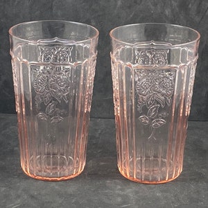 May include: Two clear pink glass tumblers with a floral design. The glasses have a textured, ribbed surface.