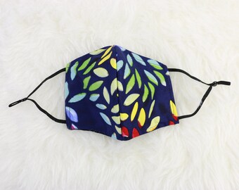 May include: A blue face mask with a colorful abstract pattern of leaves. The mask has black elastic ear loops.