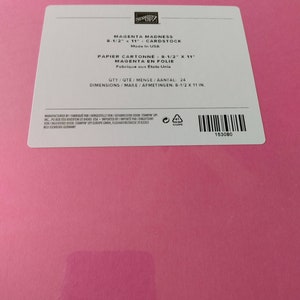 May include: A pack of Magenta Madness cardstock by Stampin' Up! with a white label. The label reads: Magenta Madness 8-1/2 x 11 Cardstock, Made in USA, Qty 24, Dimensions 8-1/2 x 11 in. The bright pink paper is visible beneath the rectangular label.