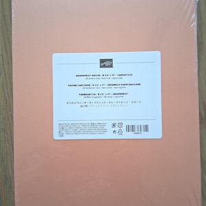 May include: A pack of 24 sheets of Grapefruit Grove cardstock measuring 8-1/2 inches by 11 inches. The paper is wrapped in clear plastic and features a white label with the Stampin' Up! logo, product name, and manufacturing details.