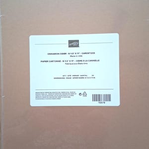 May include: A pack of 24 sheets of Cinnamon Cider cardstock in a clear plastic wrapper. The white label displays the Stampin' Up! logo, the product name, and dimensions of 8-1/2 inches by 11 inches, along with a barcode and manufacturing details.