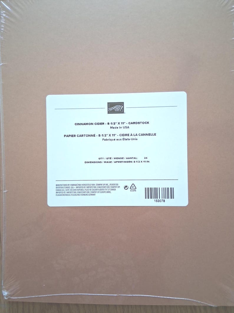 May include: A pack of 24 sheets of Cinnamon Cider cardstock in a clear plastic wrapper. The white label displays the Stampin' Up! logo, the product name, and dimensions of 8-1/2 inches by 11 inches, along with a barcode and manufacturing details.
