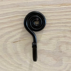 May include: A black metal hook with a spiral design. The hook is mounted on a wooden surface.