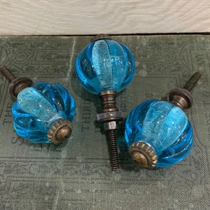 May include: Three blue glass cabinet knobs with a ribbed design and a brass base.