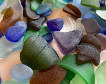 May include: A collection of colorful sea glass in various shapes and sizes. The glass is smooth and polished, with shades of blue, green, purple, brown, and white.