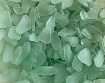 May include: A close-up view of a large pile of sea glass, all in a light green color. The glass pieces are smooth and have been tumbled by the ocean.