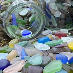 May include: A glass jar filled with colorful sea glass pieces. The sea glass is in various shapes and sizes, including small, medium, and large pieces. The sea glass is a mix of colors, including blue, green, brown, and white.