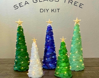 Peut inclure: Cinq kits de bricolage d'arbres en verre de mer verts, bleus et blancs, chacun surmonté d'une étoile de mer. Les arbres sont ornés de guirlandes lumineuses. Le texte "SEA GLASS TREE DIY KIT" est en haut.