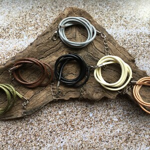 May include: A set of six different colored cords with metal clasps. The cords are arranged in a circle on a piece of driftwood.