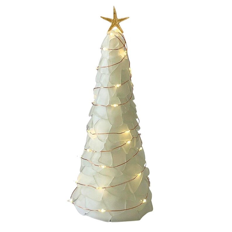 May include: A decorative Christmas tree made of white glass pieces, adorned with warm white lights and a gold starfish topper. The tree has a conical shape and is wrapped with copper wire lights.