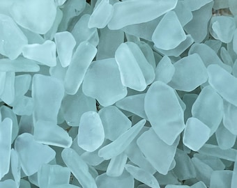May include: A close-up of a pile of frosted sea glass, with a light blue color. The glass is smooth and has been tumbled by the ocean.
