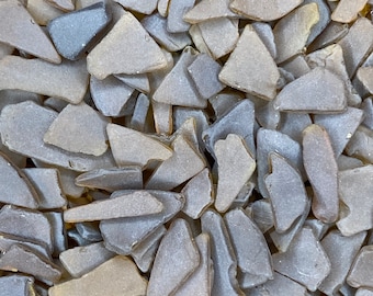 May include: A close-up of a pile of small, irregular pieces of sea glass in shades of brown and gray.