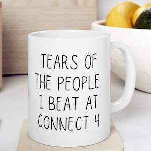 May include: White ceramic coffee mug with black text that reads "Tears of the people I beat at Connect 4".