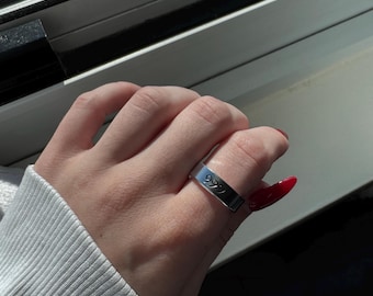 May include: A silver ring with the number "999" engraved on it. The ring is worn on a finger with red nail polish.