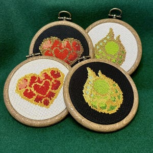 Può includere: Quattro telai da ricamo a punto croce con cornici in legno. Due telai presentano disegni a cuore rosso su sfondi neri e bianchi. Gli altri due telai mostrano un disegno di gemma verde e oro. Ogni telaio ha un anello di metallo per appenderlo.