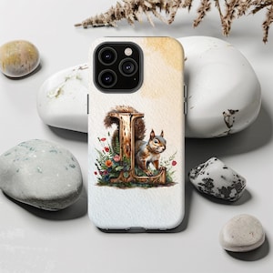 May include: A white phone case featuring a watercolor design with the letter "L" in a wooden style, adorned with a squirrel and floral elements. The case has a light background with a watercolor wash.