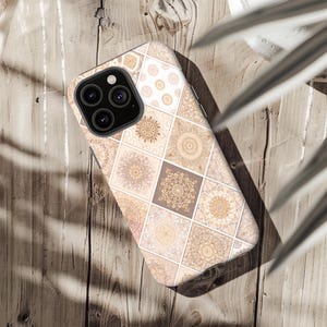 Könnte beinhalten: Eine Handyhülle mit einem geometrischen Muster aus beige, braunen und braunen Quadraten. Jedes Quadrat weist ein anderes Mandala-Design auf. Die Handyhülle hat ein schwarzes Kameramodul und liegt auf einer Holzoberfläche.