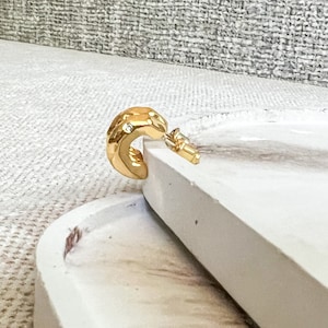 May include: Gold hoop earrings with a textured finish and small clear stones. The earrings are on a white surface.