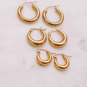 May include: Set of four gold hoop earrings of varying sizes. The earrings are all made of a thick, round wire.