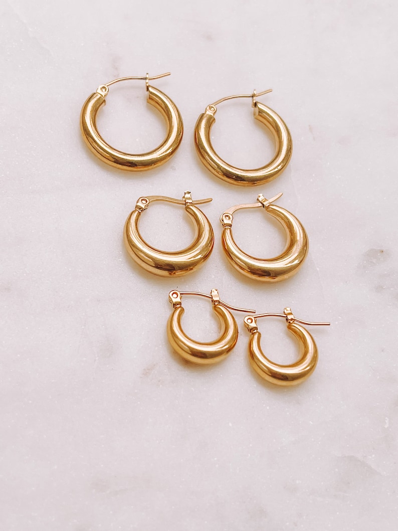 May include: Set of four gold hoop earrings of varying sizes. The earrings are all made of a thick, round wire.