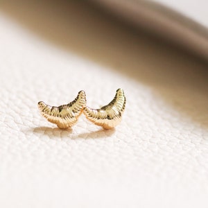 May include: A pair of gold crescent moon shaped earrings. The earrings are textured and have a delicate, feminine look.