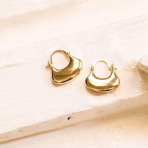 May include: A pair of gold hoop earrings with a unique, slightly curved, and slightly rounded shape.