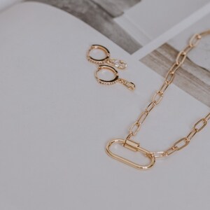 以下が含まれることがあります： カラビナ留めの金色のチェーンネックレスと、小さなダイヤモンドのアクセントが付いた2つの金色のフープイヤリング