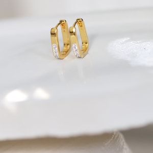 Peut inclure: Une paire de boucles d'oreilles créoles en or avec une rangée de petites pierres claires sur chaque créole.