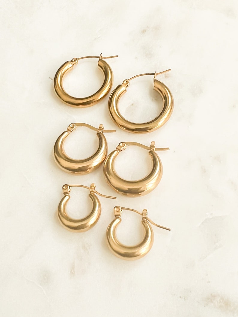May include: Set of four gold hoop earrings of varying sizes. The earrings are all made of a thick, smooth metal and have a simple, classic design.