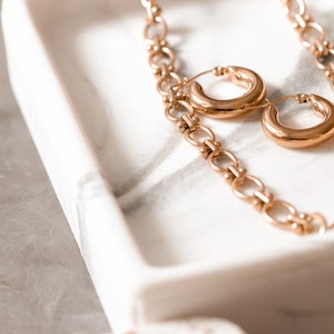 May include: A gold chain necklace with two large gold hoop earrings on a white marble tray.
