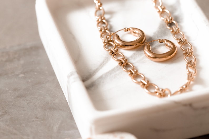 May include: A gold chain necklace with two large gold hoop earrings on a white marble tray.
