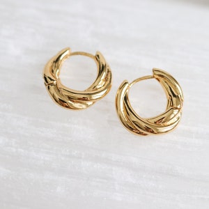 May include: A pair of gold hoop earrings with a twisted design. The earrings are made of thick, textured metal.