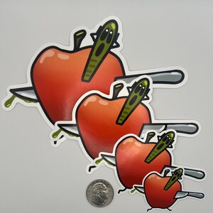 May include: Set of four stickers featuring red apples pierced by knives. The apples have green stems and are dripping green liquid. The knives are silver with black handles. The stickers vary in size.