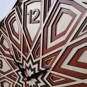 May include: A wooden clock with a geometric design in shades of brown and white. The clock face features a large number "12" and black hands.
