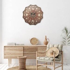 May include: A wooden clock with a geometric design in shades of brown and beige. The clock face features Roman numerals and is surrounded by a decorative border. The clock is hanging on a white wall in a room with a wooden dresser and a chair.