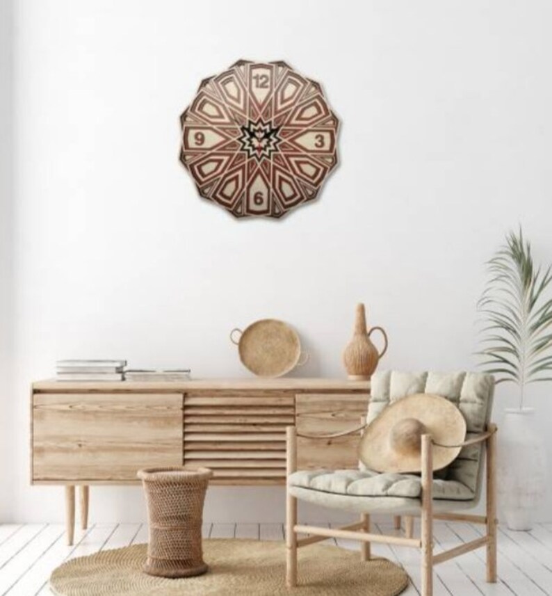 May include: A wooden clock with a geometric design in shades of brown and beige. The clock face features Roman numerals and is surrounded by a decorative border. The clock is hanging on a white wall in a room with a wooden dresser and a chair.