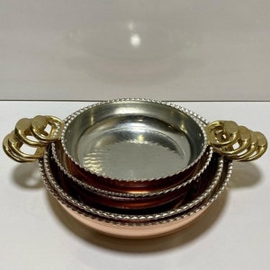 K&ouml;nnte beinhalten: Set aus drei Kupferschalen mit geh&auml;mmerter Oberfl&auml;che und Messinggriffen. Die Schalen sind ineinander verschachtelt und haben einen perlenbesetzten Rand.