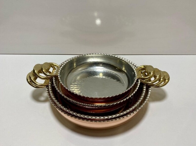 K&ouml;nnte beinhalten: Set aus drei Kupferschalen mit geh&auml;mmerter Oberfl&auml;che und Messinggriffen. Die Schalen sind ineinander verschachtelt und haben einen perlenbesetzten Rand.