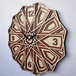 May include: A wooden clock with a geometric design in shades of brown and red. The clock face features Roman numerals for the hours and a starburst design in the center.