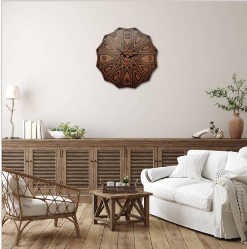 May include: A brown wooden clock with a geometric design and black Roman numerals. The clock is hanging on a white wall above a wooden cabinet and a white couch.