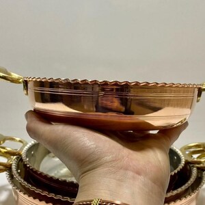 K&ouml;nnte beinhalten: Ein Satz aus drei Kupferservier-Schalen mit goldenen Griffen. Die Schalen sind ineinander verschachtelt und haben einen dekorativen gewellten Rand.